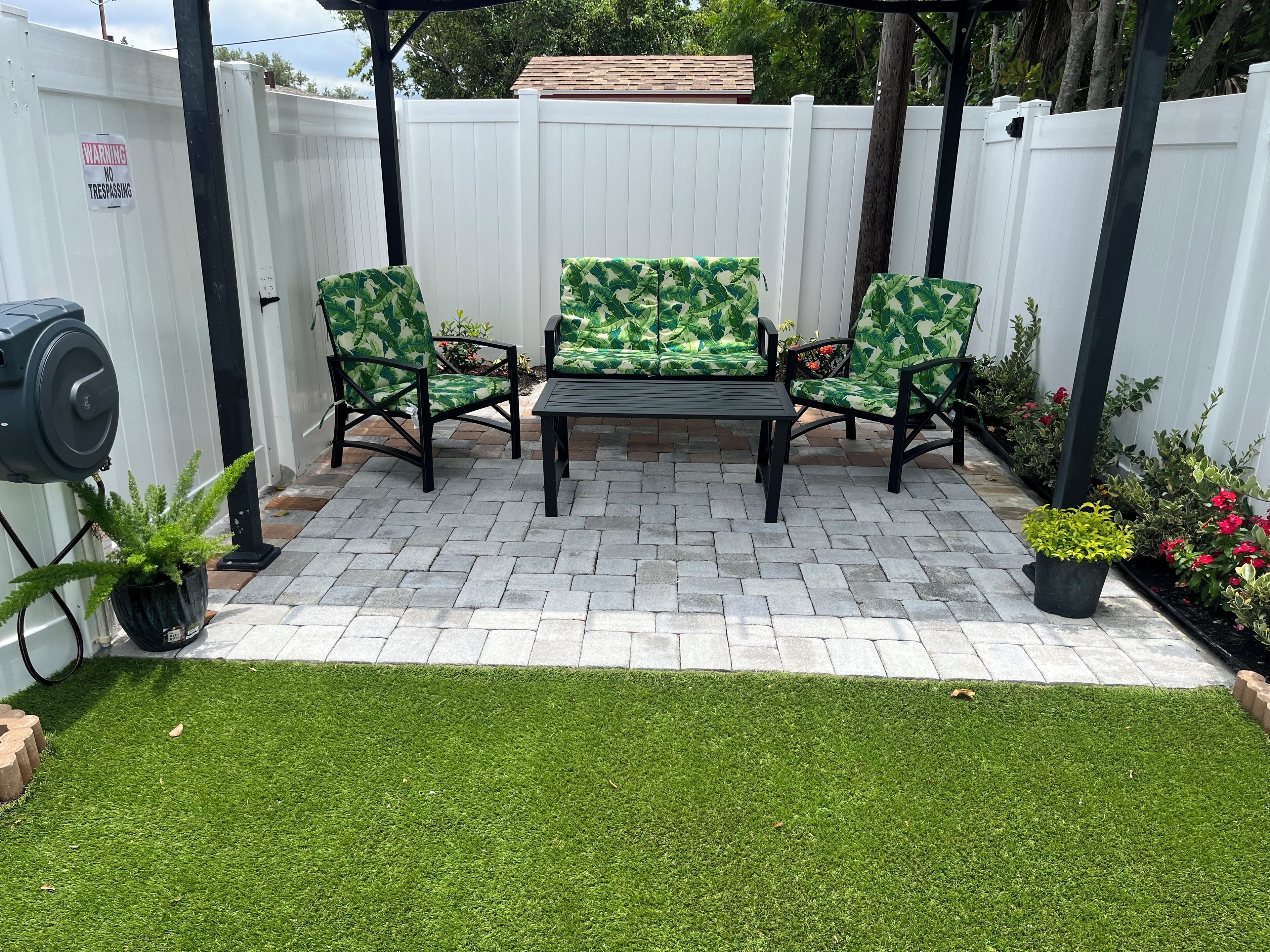 Une terrasse avec une clôture blanche, deux chaises, une table et des plantes en pot.