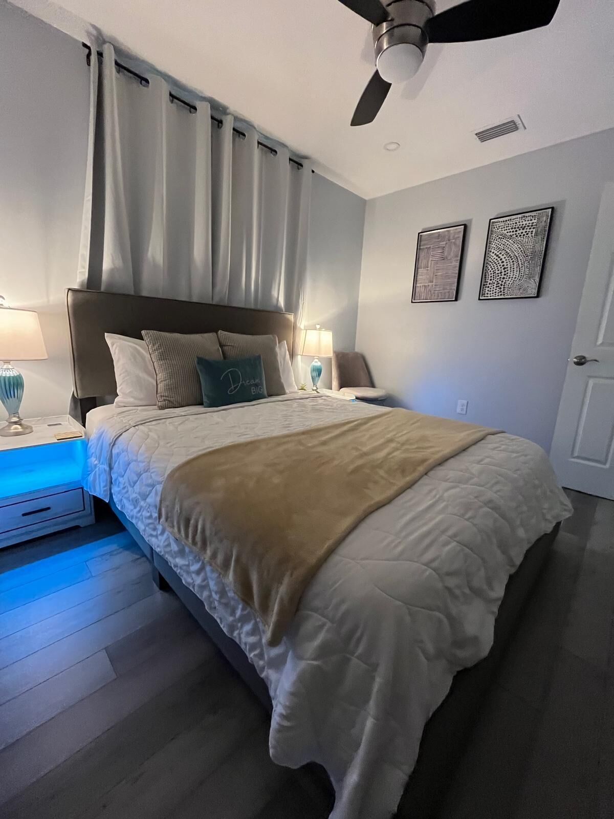 A bedroom with a bed, two bedside tables with lamps, a ceiling fan, and two wall art pieces.