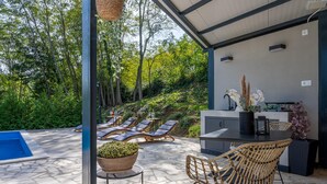 A covered outdoor area with a pool, lounge chairs, a dining table with chairs, and a potted plant. - Villa InSa (Pican)