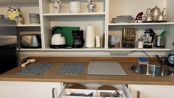 Una cocina con encimera de madera, un tostador, un hervidor, una cafetera y diferentes utensilios de cocina en estantes.