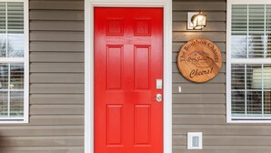 Uma porta vermelha com moldura branca, uma luminária acima dela e uma placa circular na parede.