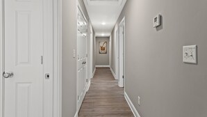 Um corredor com portas brancas, piso de madeira e luminária no teto.