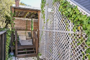 Una terraza de madera con un alfombra estampado de cebra, una valla blanca de celosía y follaje.