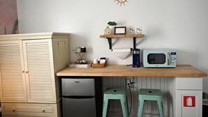 A compact kitchen with a microwave, a small refrigerator, a wooden table with a shelf, and two stools. - The Dylan Suites 5- Comfortable Stay Near Downtown St. Augustine & Flagler (St. Augustine)