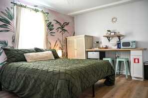 A bedroom with a bed, a desk, a microwave, and a small kitchenette.