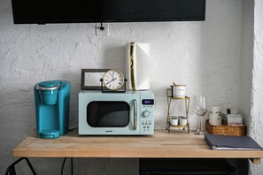 A kitchenette with a coffee maker, microwave, clock, and a small shelf with kitchenware.