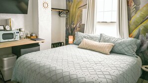 Ein Schlafzimmer mit einem Bett, einem Schreibtisch mit Mikrowelle, einem kleinen Kühlschrank, einer Pendelleuchte und einem Fenster mit Vorhängen.