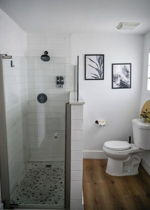 Ein Badezimmer mit Dusche, Toilette und zwei gerahmten Bildern an der Wand.