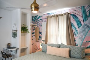 Ein Schlafzimmer mit Bett, Schreibtisch, Stuhl, einer hängenden Pflanze und einem Deckenventilator.