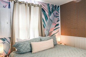 Un dormitorio con cama, almohadas, cortinas, una pared con diseño de hojas y un panel de pared de madera.