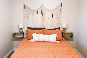Un lit avec une couette orange, deux oreillers, une tête de lit en macramé et des lampes de chevet.