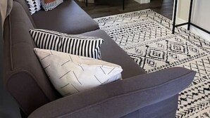 A living room with a sofa, a chair, a patterned rug, and a television on the wall. - Cozy Getaway Steps from Historic Downtown with Parking (St. Augustine)