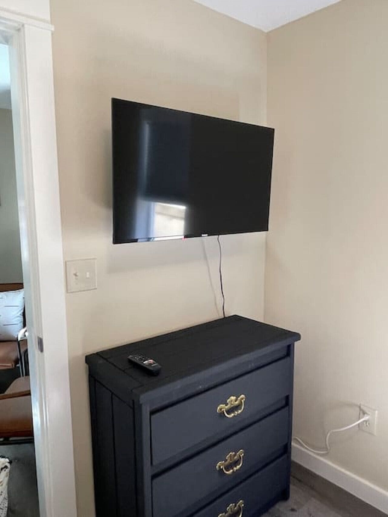 Une pièce dotée d’un téléviseur à écran plat fixé au mur, au-dessus d’une commode de couleur sombre comportant trois tiroirs.
