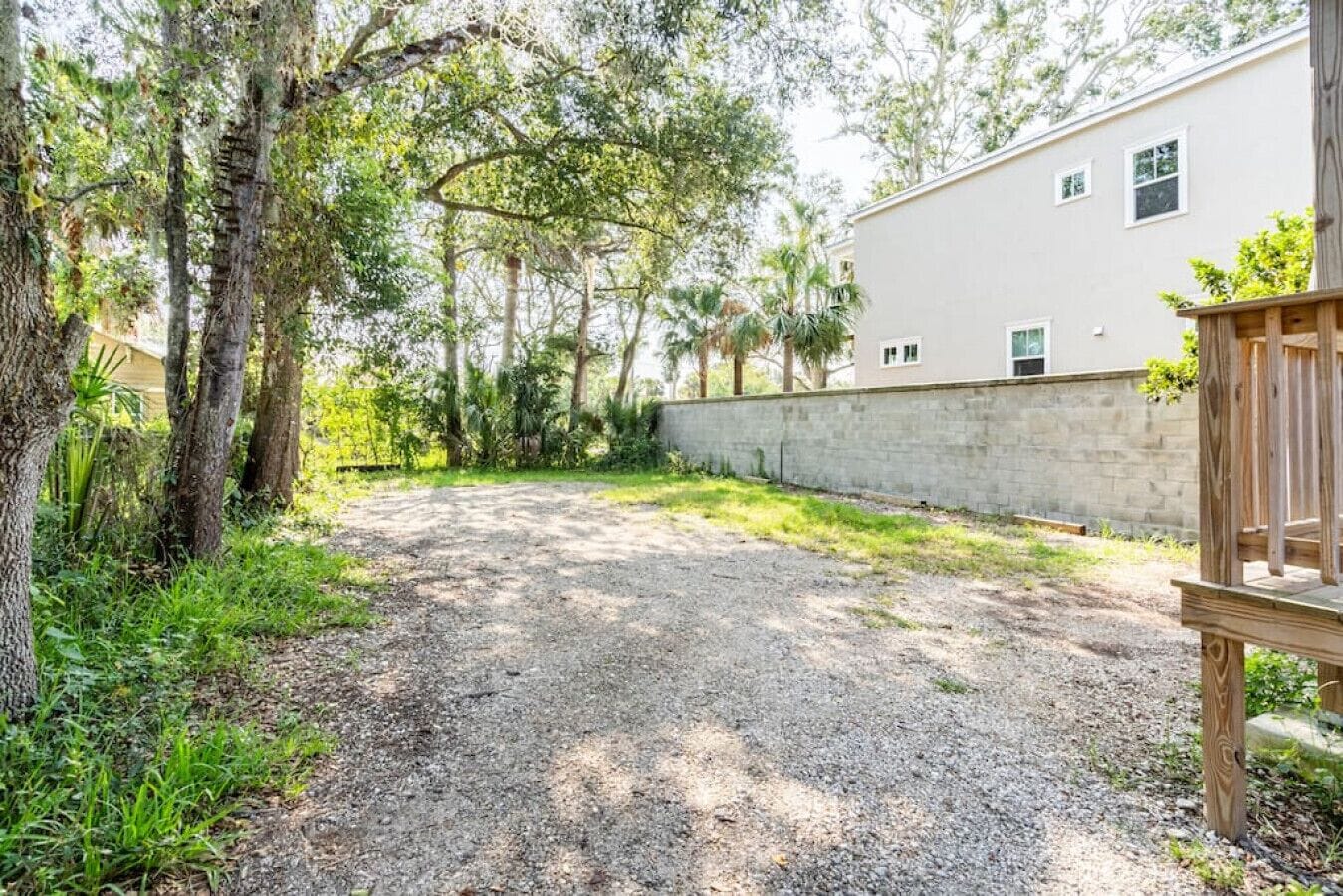 A gravel driveway leading to a white building with a stone wall, surrounded by trees and greenery.