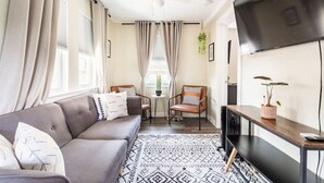 A modern living room with a grey sofa, a black TV stand, a patterned rug, and a ceiling fan. - Cozy Getaway Steps from Historic Downtown with Parking (St. Augustine)