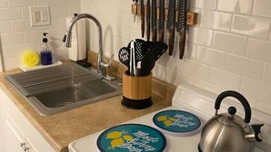 Cocina con alacenas blancas, un lavamanos de acero inoxidable y una estufa con tres posavasos azules.