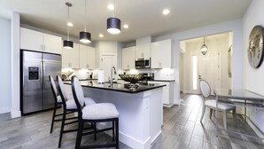 Una cocina moderna con electrodomésticos de acero inoxidable, una isla central con asientos e iluminación colgante.