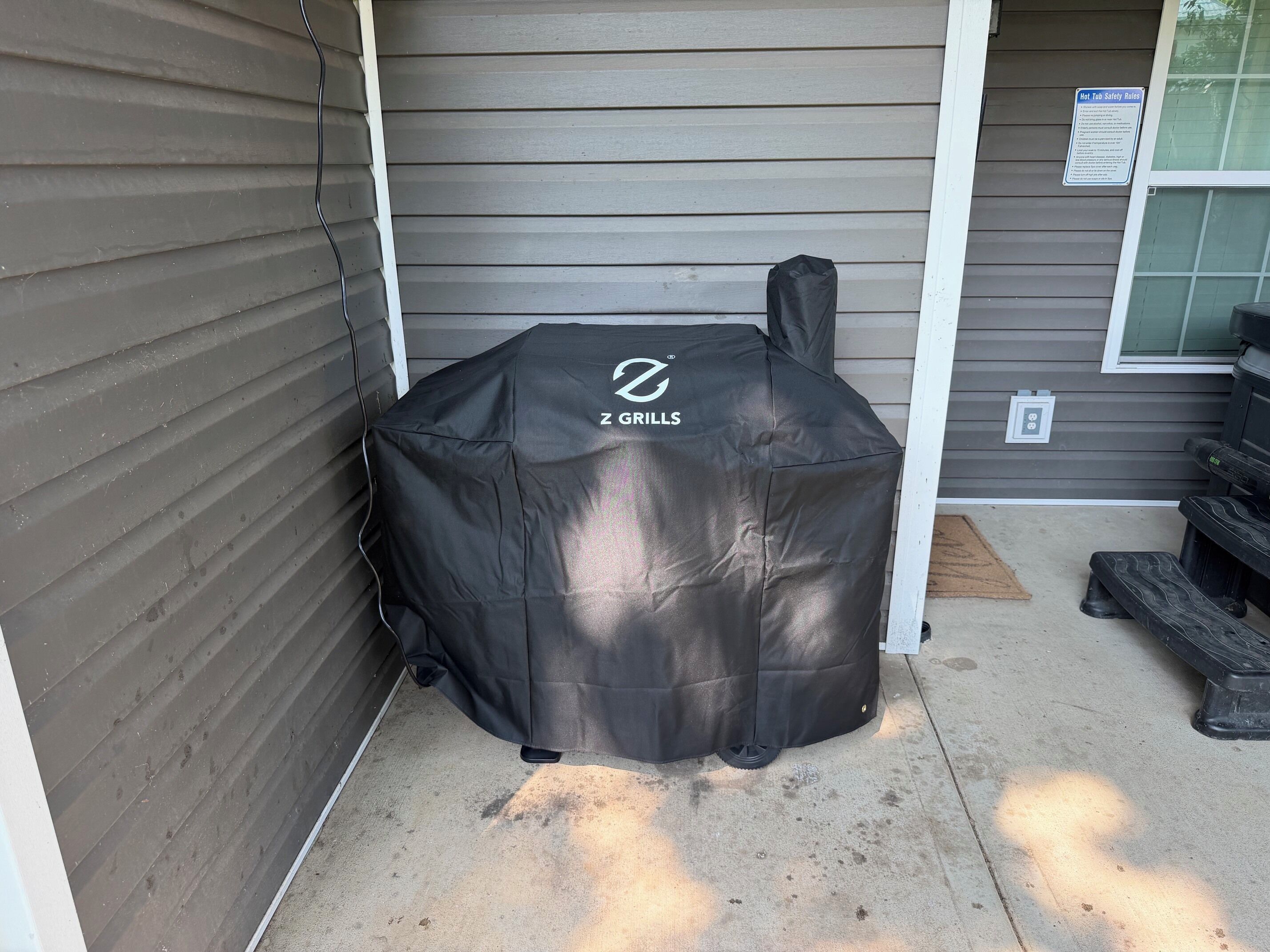 A covered grill with a brand logo, a window with a safety sign, and a concrete patio.