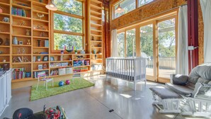 Una stanza spaziosa con soffitto alto, scaffali in legno, una culla bianca e un'ampia finestra che offre vista sull'esterno.
