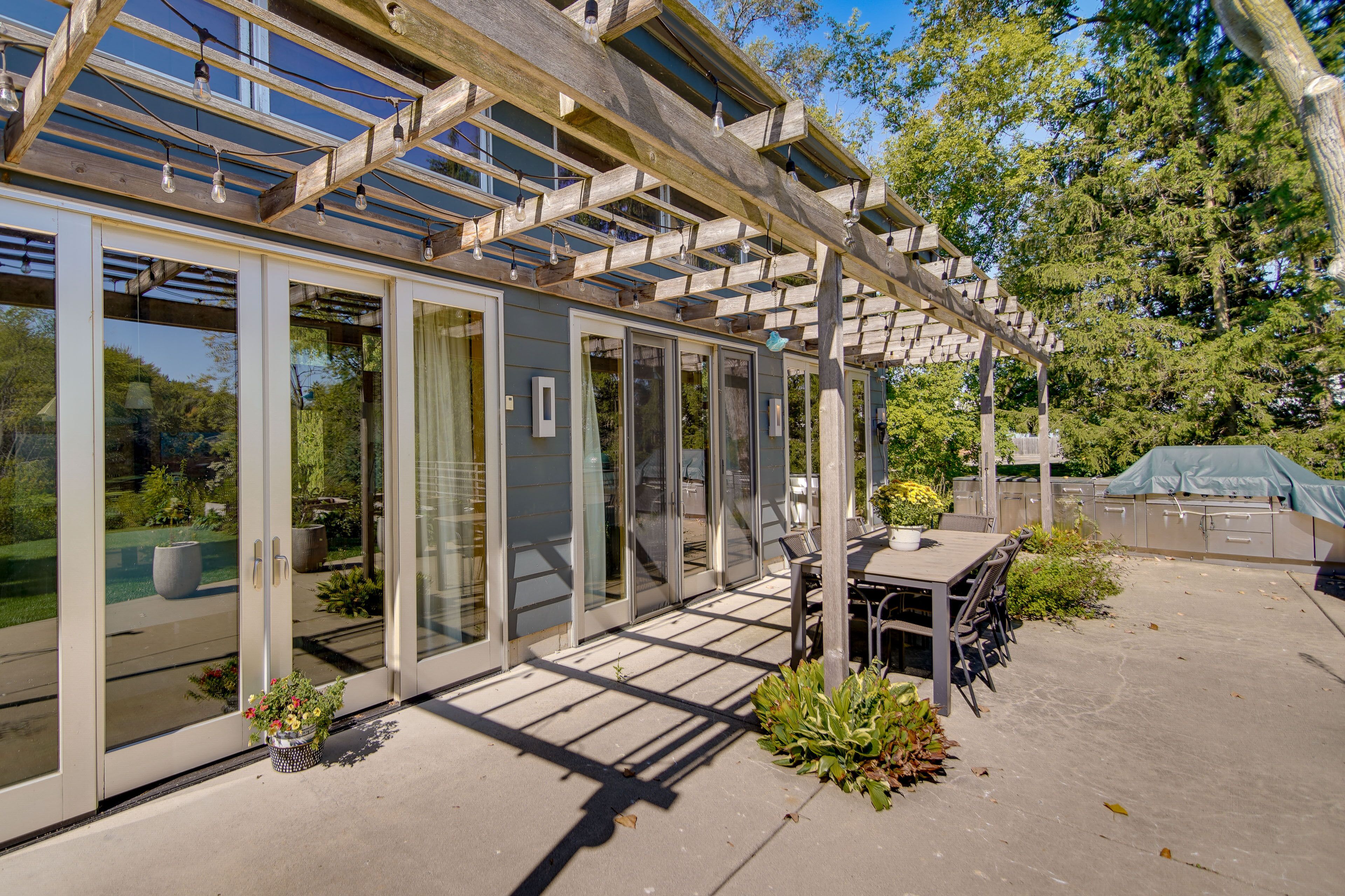 Un patio couvert avec une table et des chaises, de grandes portes-fenêtres coulissantes et une structure en forme de pergola.