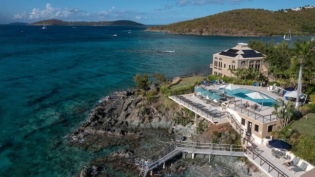 Une propriété située sur la côte, dotée d’un grand bâtiment comprenant une piscine, un quai et offrant une vue sur la mer et les collines.