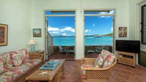 Un salon avec vue sur l’océan, des meubles en osier, un téléviseur et une table décorée d’étoiles de mer.