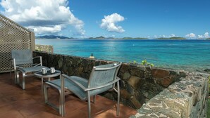 Une terrasse avec deux chaises et une table, d’où l’on peut admirer une mer bleue et limpide ainsi que des îles lointaines.