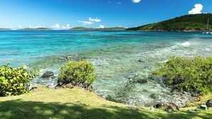 On distingue clairement une zone côtière avec un premier plan herbeux, une côte rocheuse et, au loin, une colline à la végétation clairsemée.