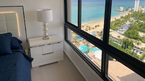 Een slaapkamer met een groot raam, met uitzicht op een strand en een resort.