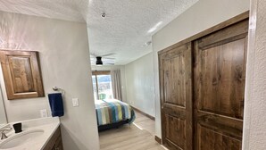 Una habitación de hotel con un armario de madera, un baño con lavamanos y espejo, y una cama con colcha a rayas.