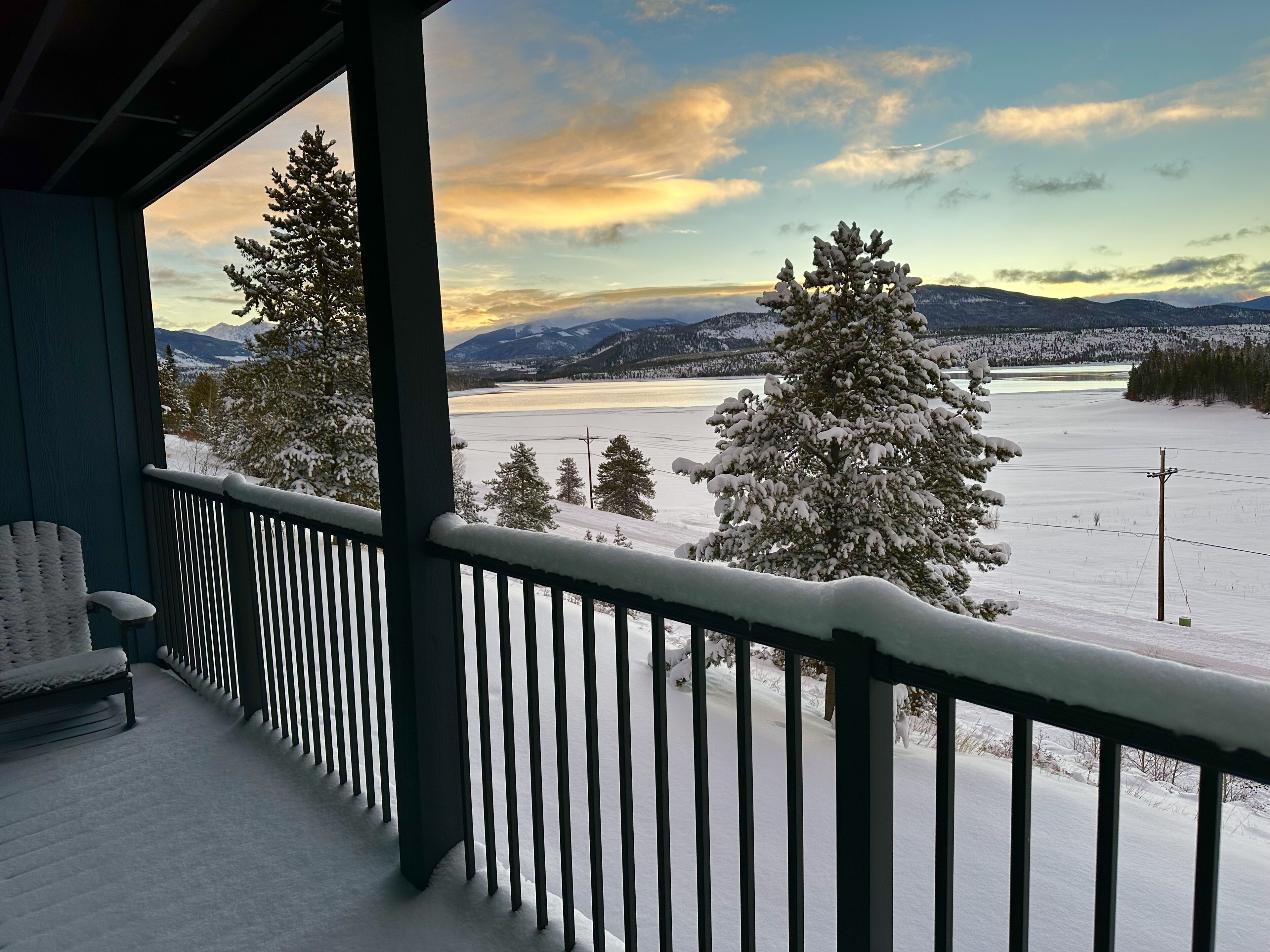Ein mit Schnee bedeckter Balkon mit Blick auf einen See und Berge.