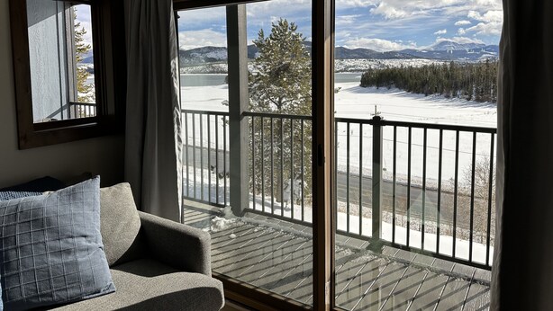 Habitación con balcón que da a un paisaje nevado, un sofá y una ventana con cortinas.