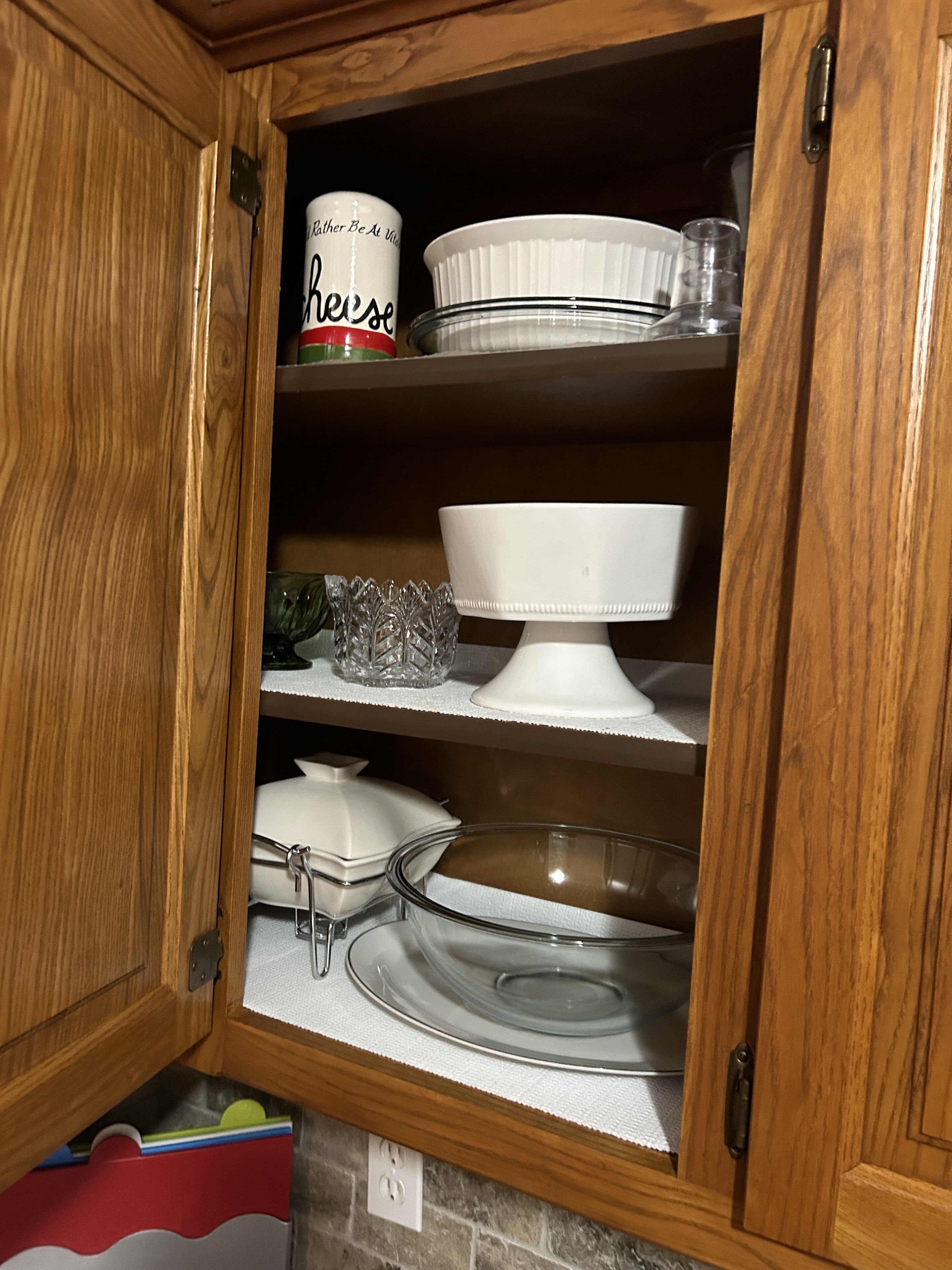 Un meuble en bois doté d’étagères contenant des ustensiles de cuisine, notamment un saladier blanc, un récipient en verre et un récipient blanc avec une étiquette.
