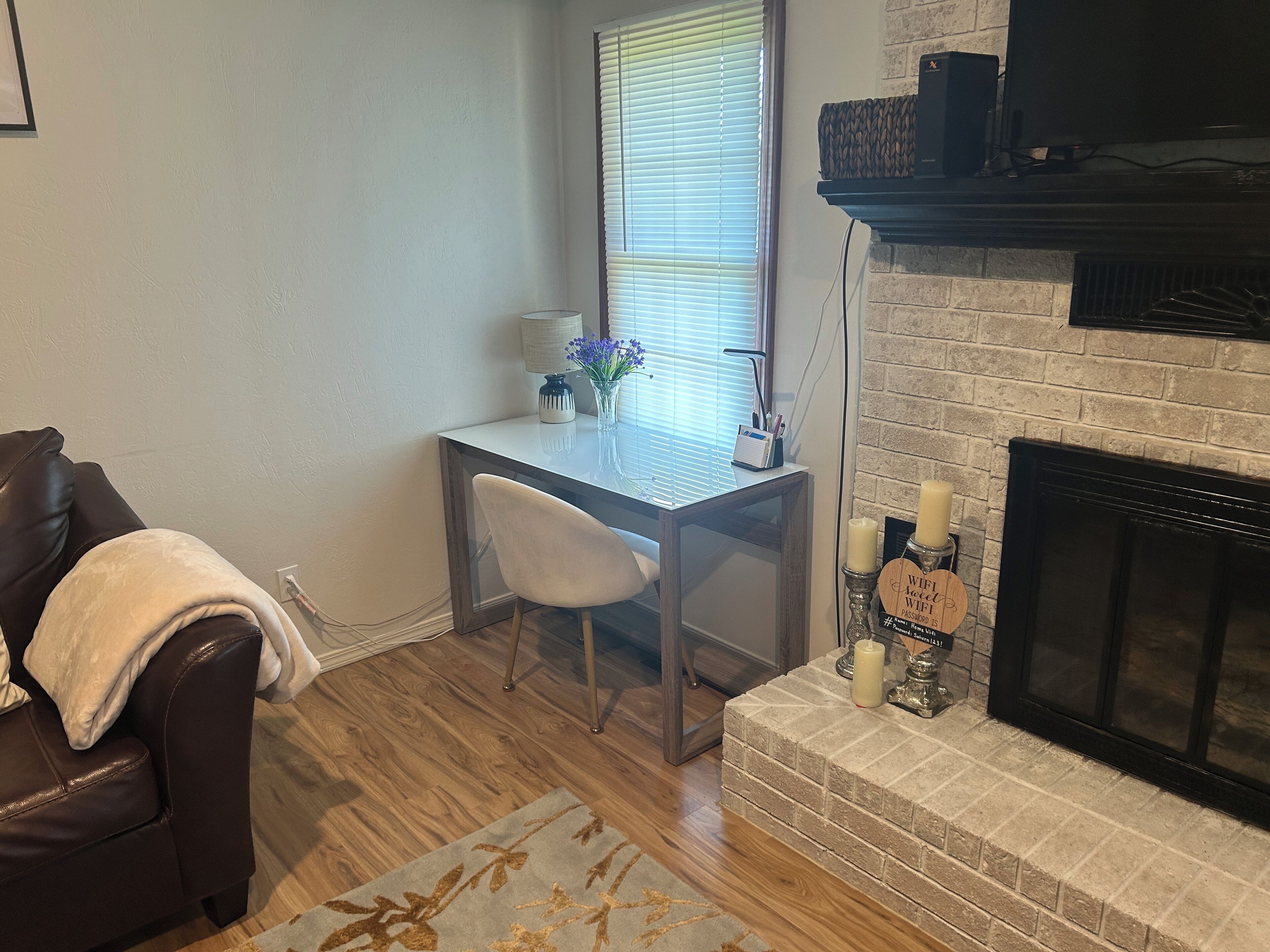 A living room with a fireplace, a dining table with chairs, a leather couch, and a window with blinds.