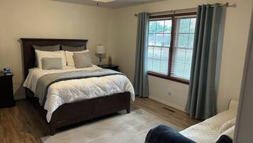 Un dormitorio con cama, mesita de noche, lámpara y ventana con cortinas.
