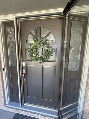 Una porta d'ingresso grigio scuro con un ghirlanda decorativa e un vetro.