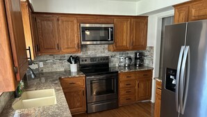A modern kitchen with wooden cabinets, stainless steel appliances, granite countertops, and a built-in oven.