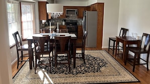 A modern kitchen with wooden cabinets, a stainless steel refrigerator, and a dining area with a patterned rug.