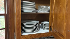 A wooden cabinet with multiple shelves containing stacked plates and a decorative bowl.