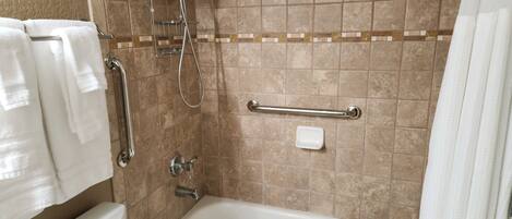 A bathroom with a bathtub, a shower, and a toilet. There is a grab bar installed near the bathtub.