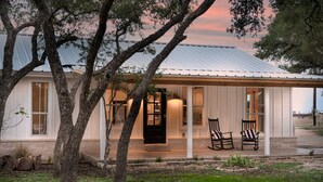 Een modern huis met een metalen dak, grote ramen en een veranda met twee stoelen.