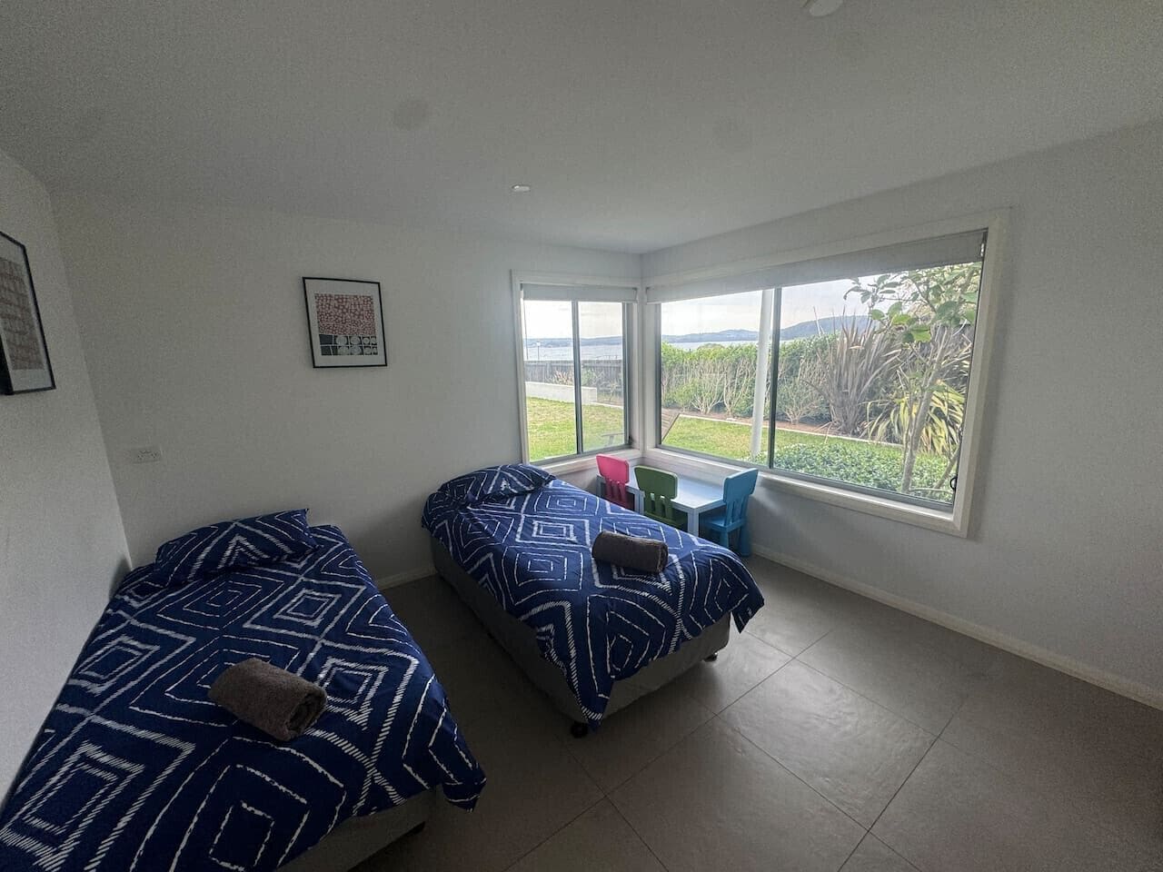 A room with two beds, a small table, and a window with a view of greenery.