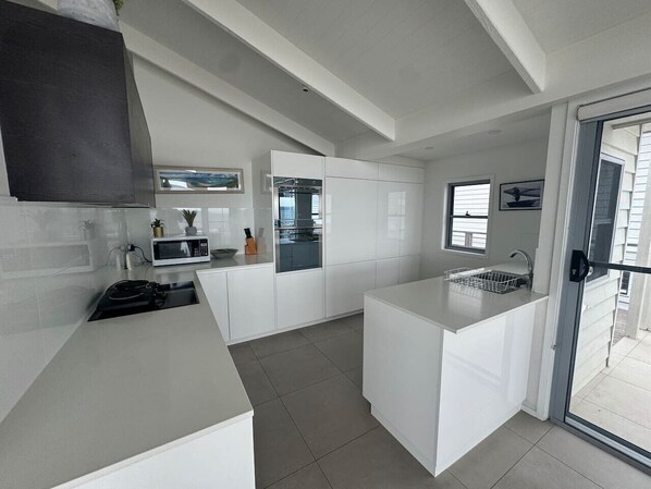 A modern kitchen with white cabinetry, a built-in oven, and a large island with a sink. - Beachside Long Beach (Long Beach)