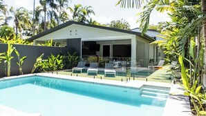 A modern pool area with clear blue water, lounge chairs, and a covered patio with glass doors.