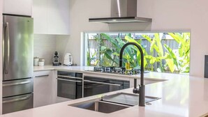 A modern kitchen with stainless steel appliances, a large window with a view of greenery, and a sleek countertop design.