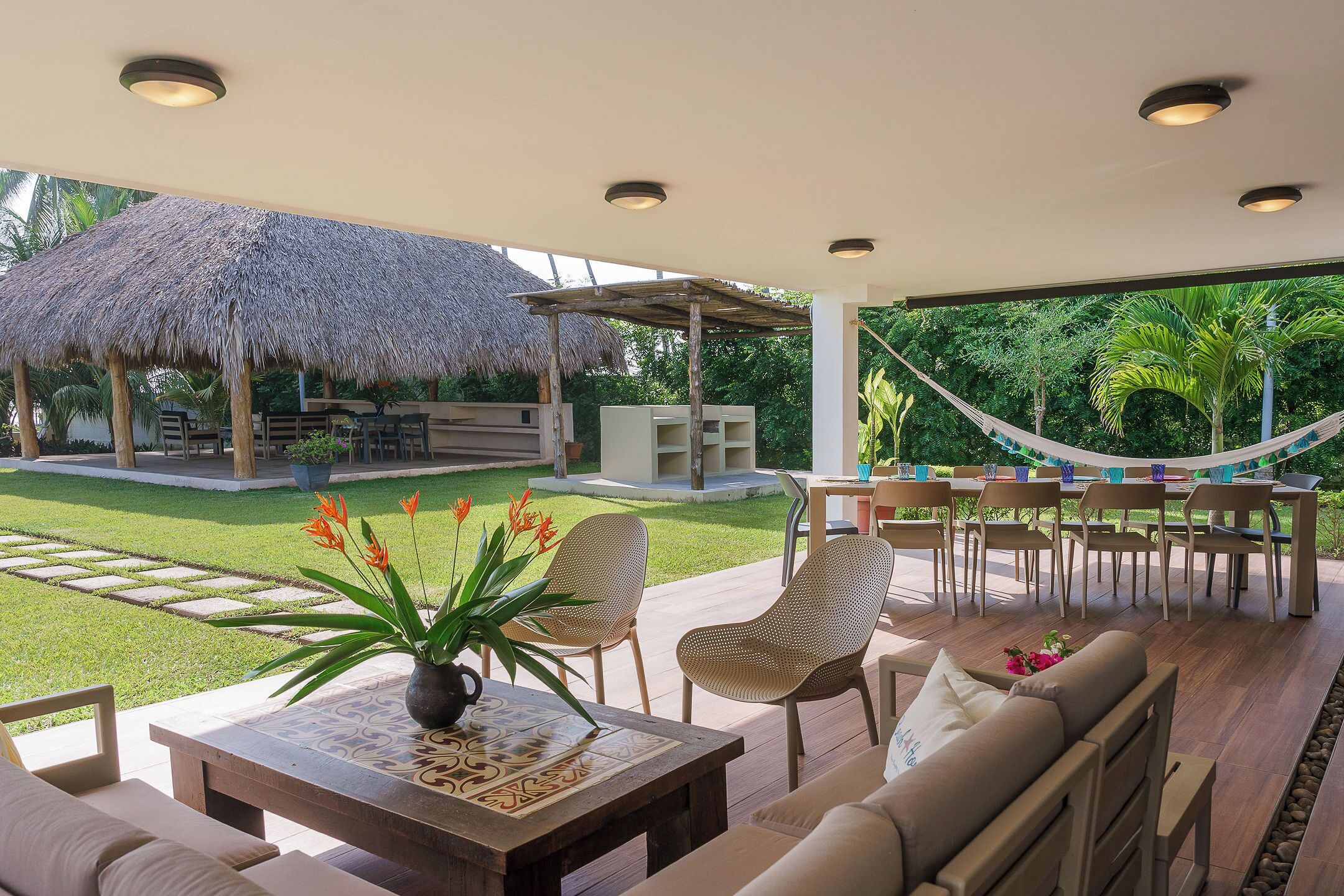 An outdoor seating area with a thatched-roof structure, a hammock, and a view of a well-maintained lawn and trees.