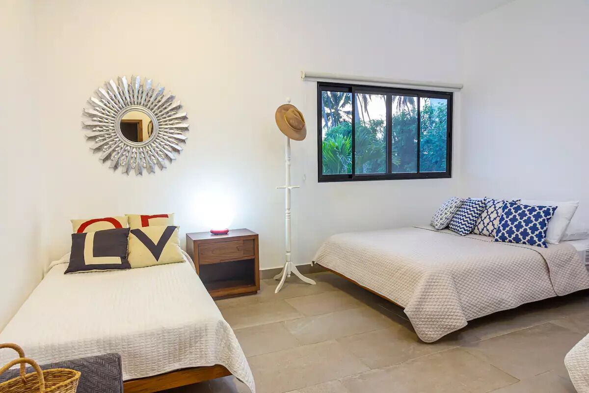 Un dormitorio con dos camas, un espejo, una ventana y una mesita de noche.