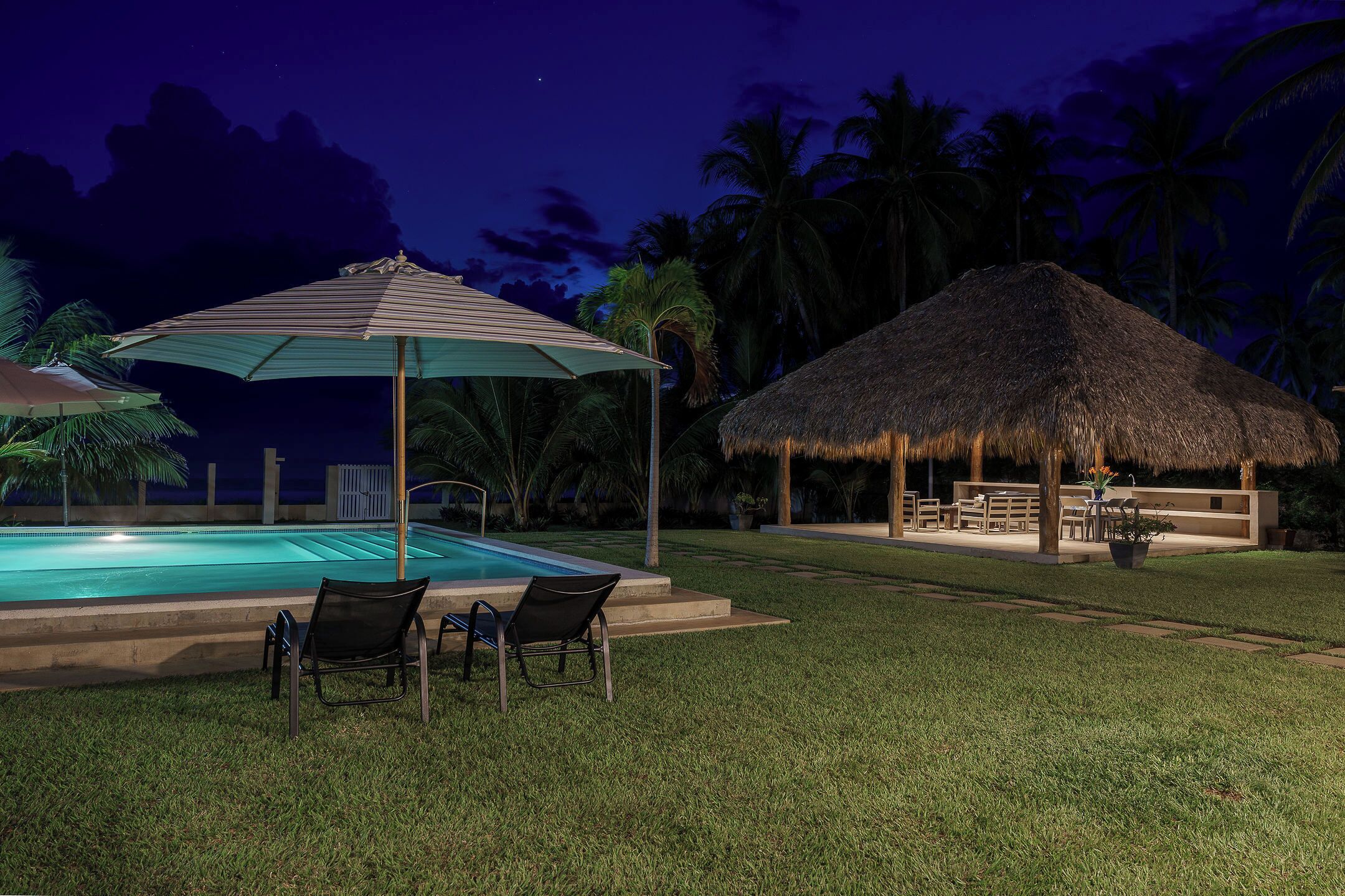 A pool area with lounge chairs and a thatched-roof structure.