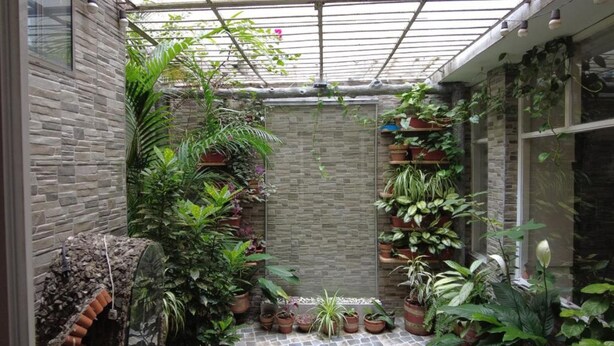 A covered garden area with stone walls, potted plants, and a brick floor. - Nora's Laureles (Medellín)