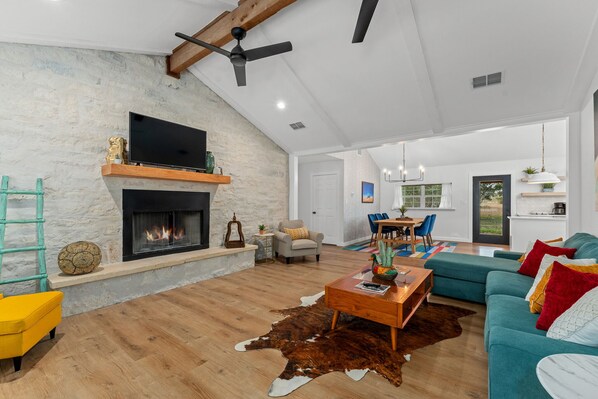 A spacious living room with a fireplace, a sofa, a coffee table, and a dining area. - Casa Blanco (Wimberley)